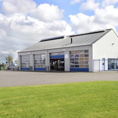 A car workshop or garage with doors open and cars on the forecourt.