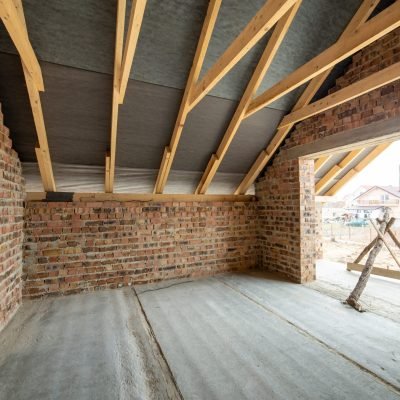 Interior of unfinished brick house with concrete floor, bare walls ready for plastering and wooden roofing frame attic under construction.